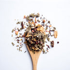 Organic herbal Acai Berry Wellness tea blend with acai berries and dried fruit pieces on wooden spoon