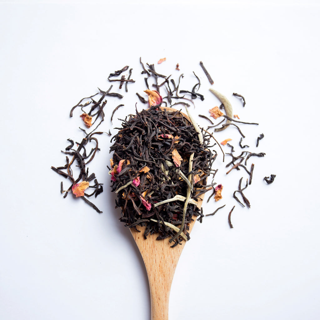 Organic herbal Herbal Sunrise tea blend with Ceylon and Assam black tea, white tea and rose petals on wooden spoon