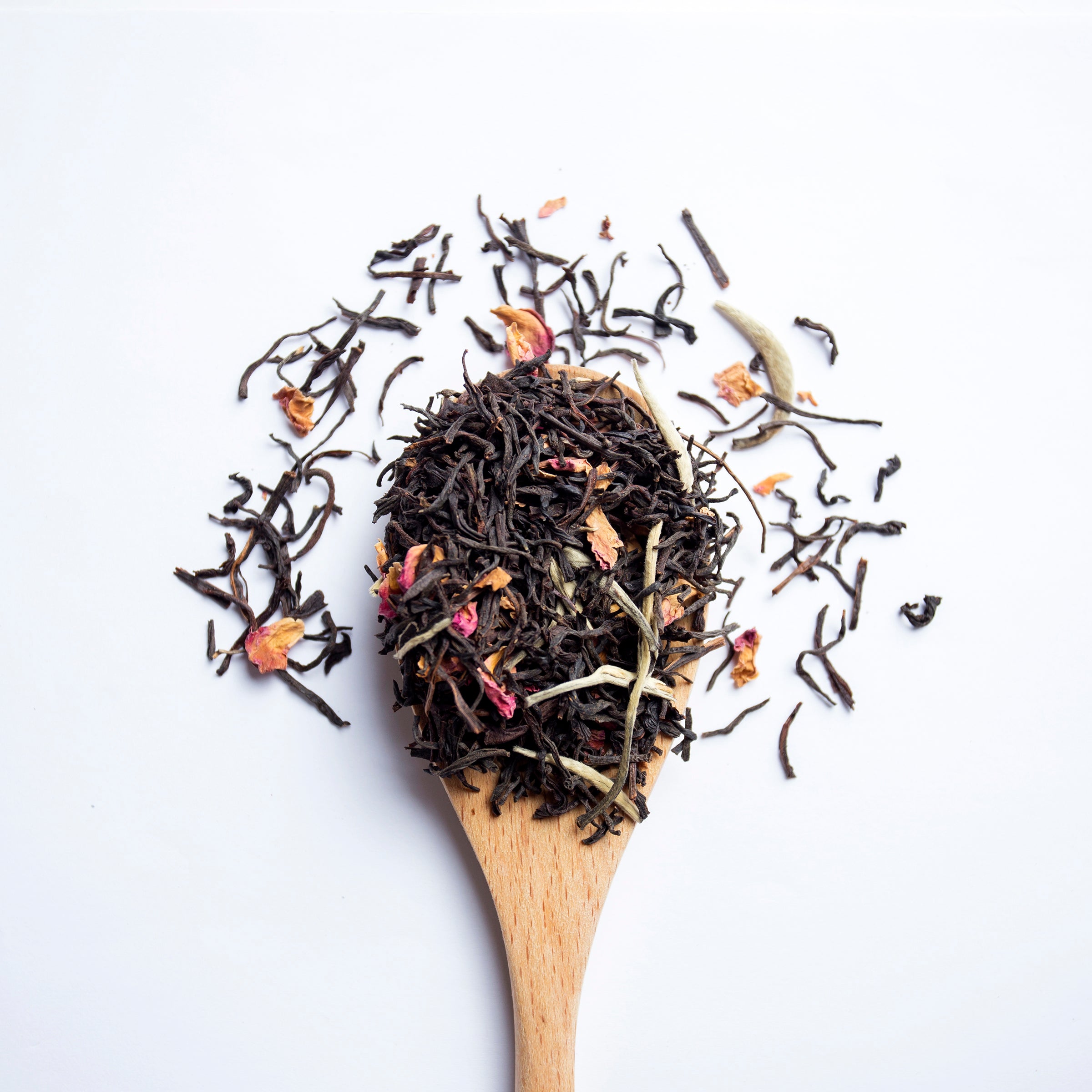 Organic herbal Herbal Sunrise tea blend with Ceylon and Assam black tea, white tea and rose petals on wooden spoon