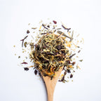 Organic herbal Slim Harmony tea blend with green tea leaves and colourful flower petals on wooden spoon