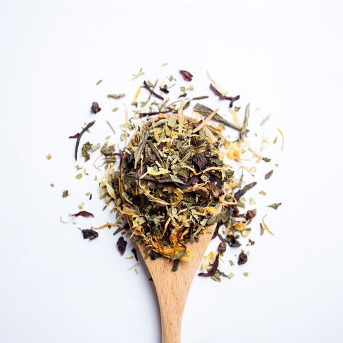 Organic herbal Slim Harmony tea blend with green tea leaves and colourful flower petals on wooden spoon